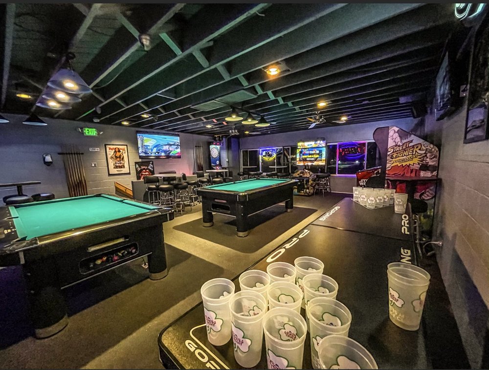 The games floor at The Blue Moon Lounge — two pool tables, a Pong PRO beer-pong table set up with cups in the foreground, and a dartboard on the back wall