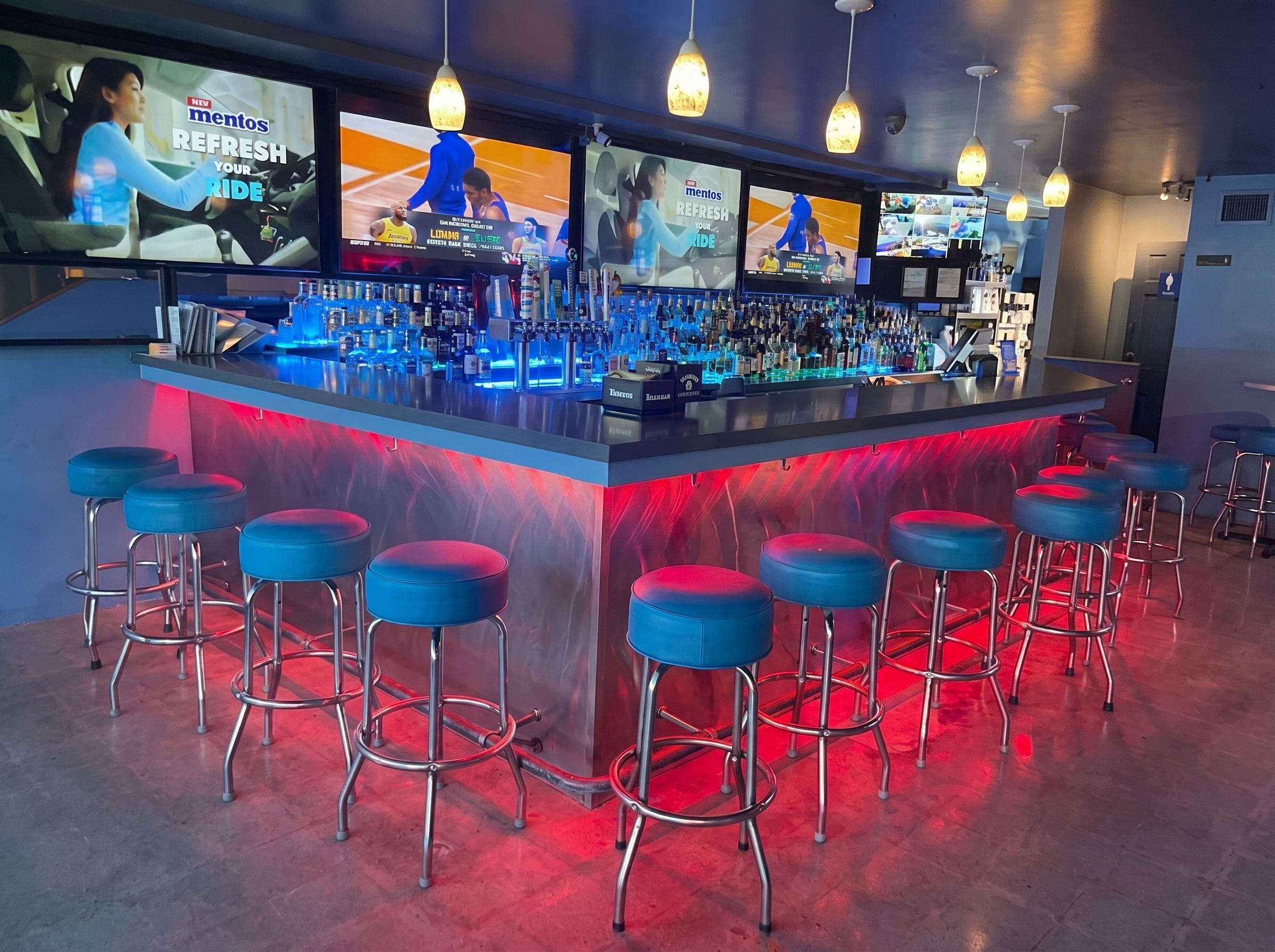 The wraparound bar at The Blue Moon, lit deep blue under the screens